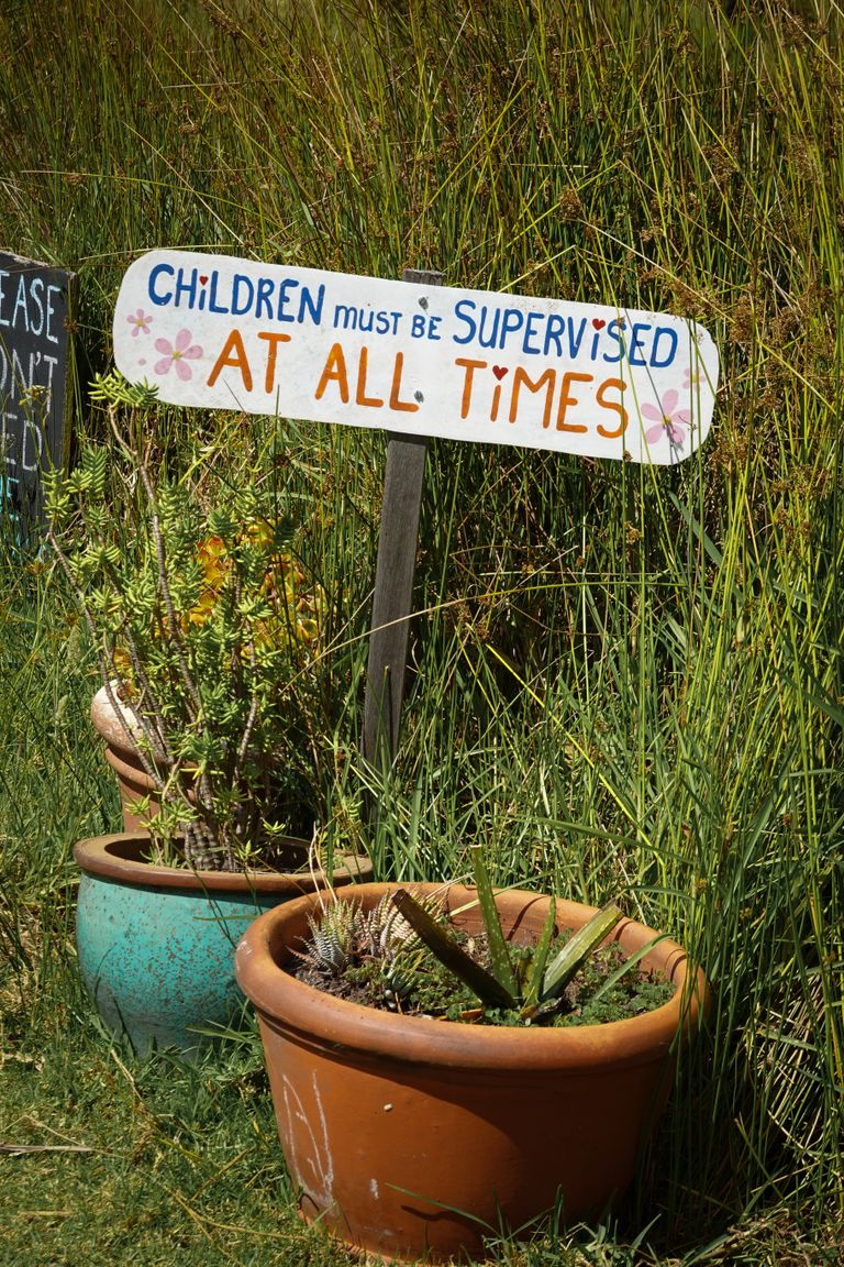 Garden sign urging child supervision amidst potted plants.